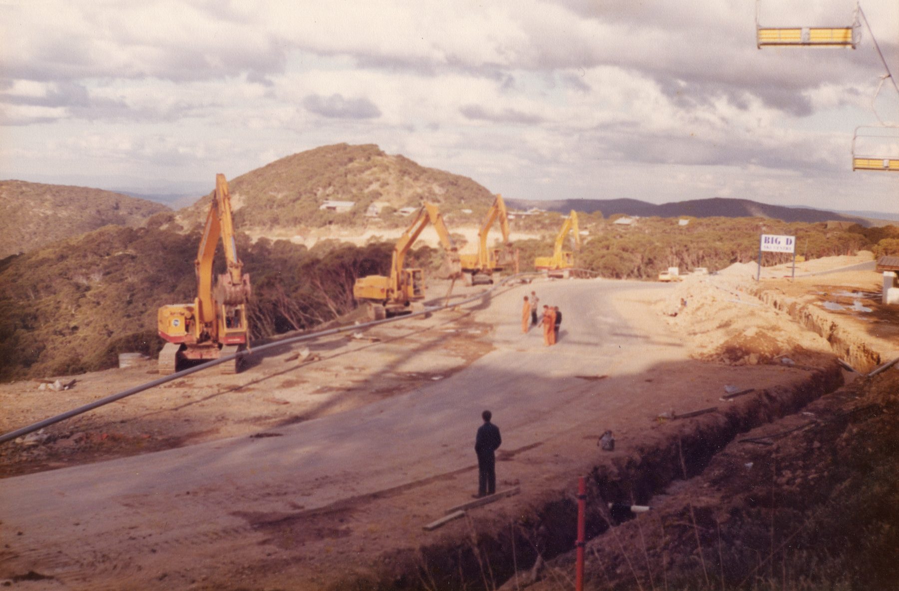 Excavator craning a services pipe into the trench, Mt Hotham, 1983